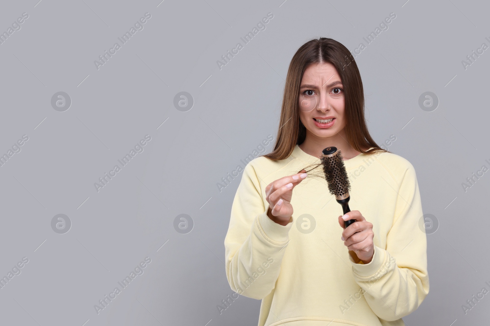 Photo of Emotional woman untangling her lost hair from brush on light grey background, space for text. Alopecia problem