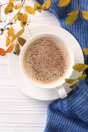 Cup of hot drink, leaves and knitted sweater on white wooden table, flat lay. Cozy autumn atmosphere