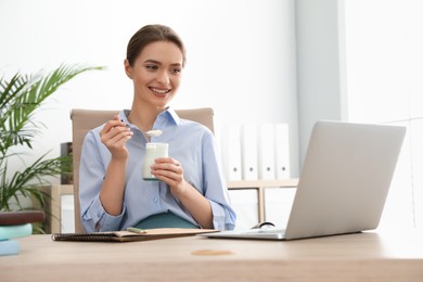 Photo of Young attractive woman with tasty yogurt at table in office