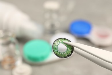 Tweezers with green contact lens over table, closeup. Space for text