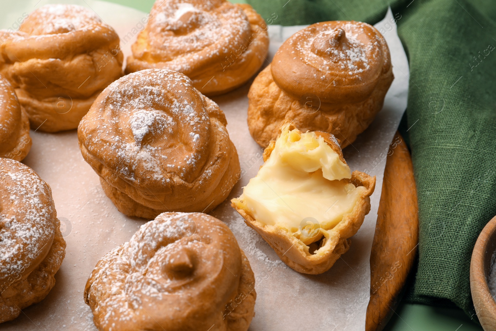 Photo of Delicious profiteroles filled with cream on green background, closeup