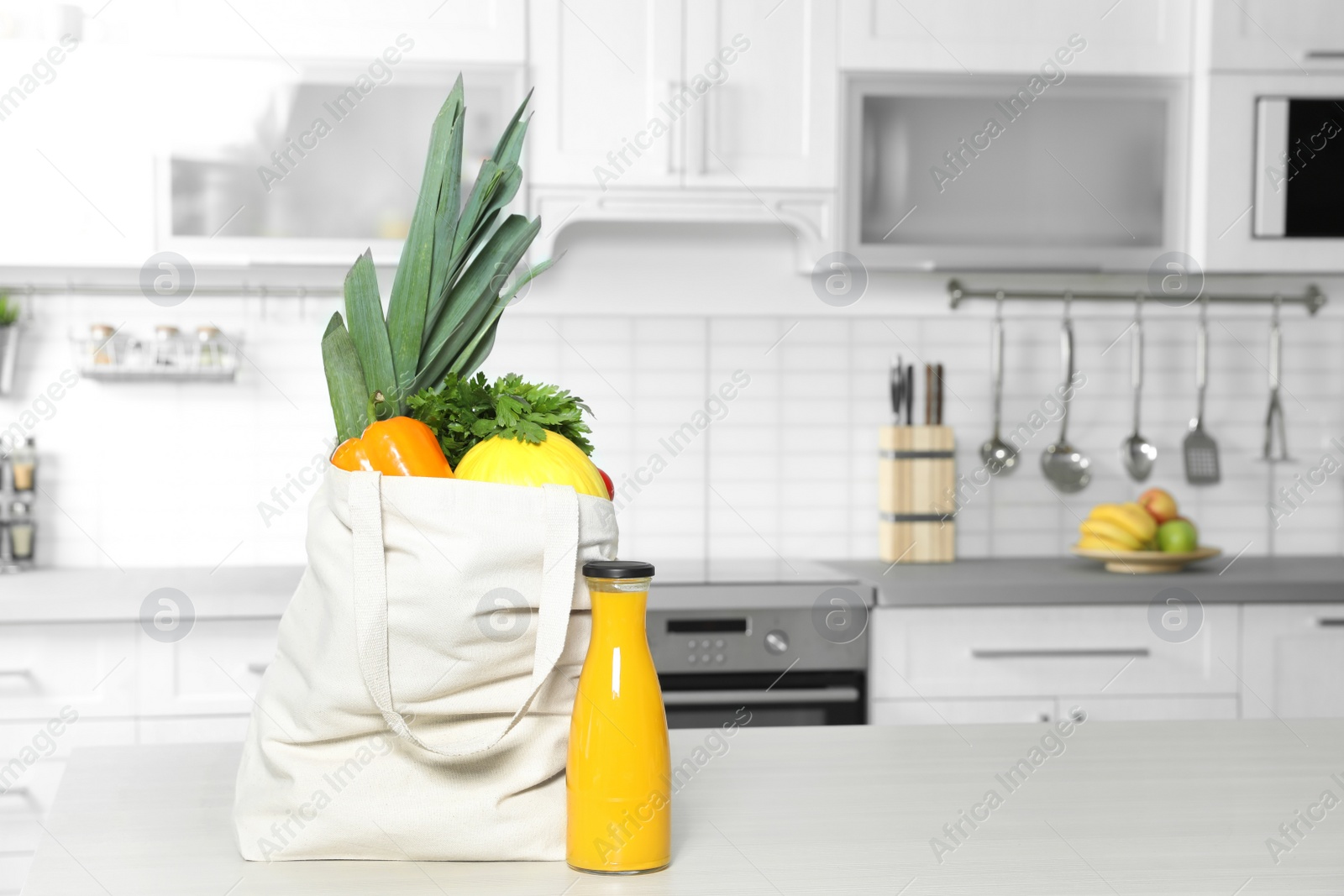 Photo of Textile shopping bag full of vegetables and juice on table in kitchen. Space for text