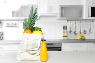 Photo of Textile shopping bag full of vegetables and juice on table in kitchen. Space for text