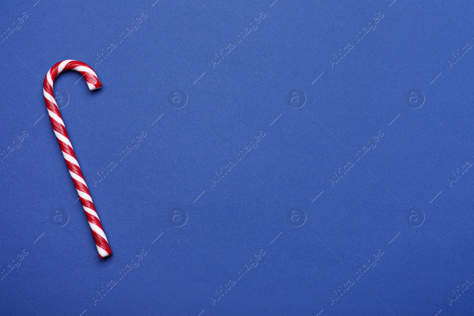 Photo of Sweet Christmas candy cane on blue background, top view. Space for text