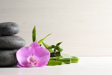 Photo of Spa stones, bamboo stems and beautiful orchid flower on white table, space for text