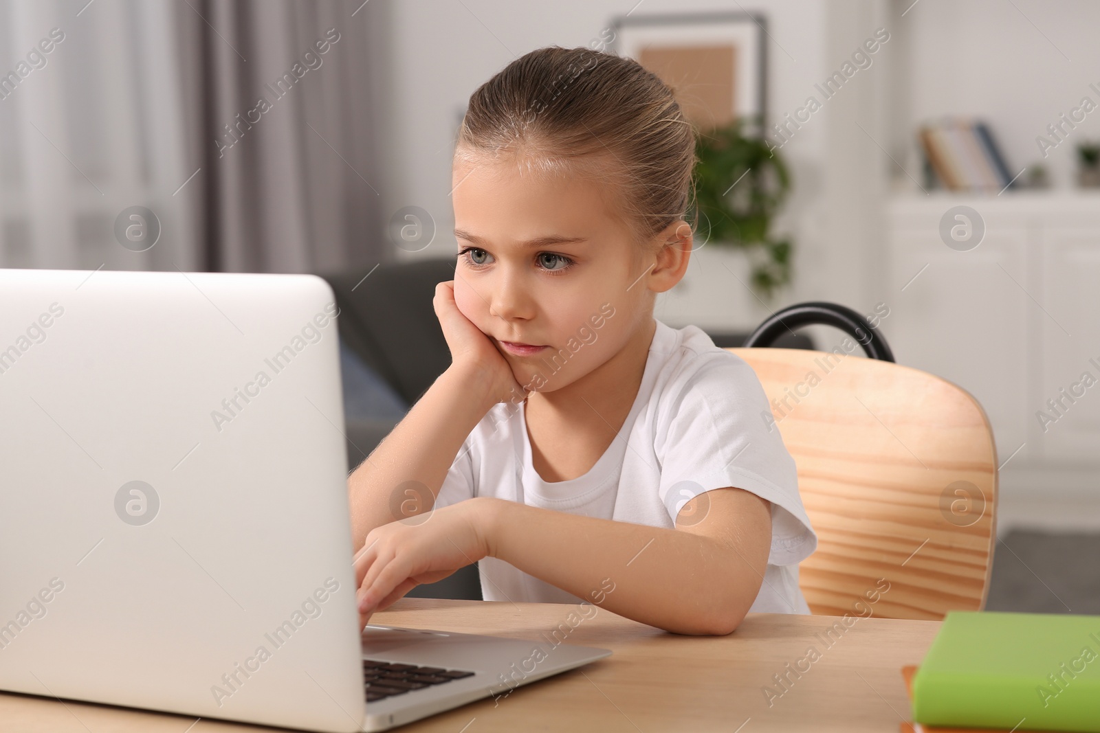 Photo of Little girl using laptop at table indoors. Internet addiction