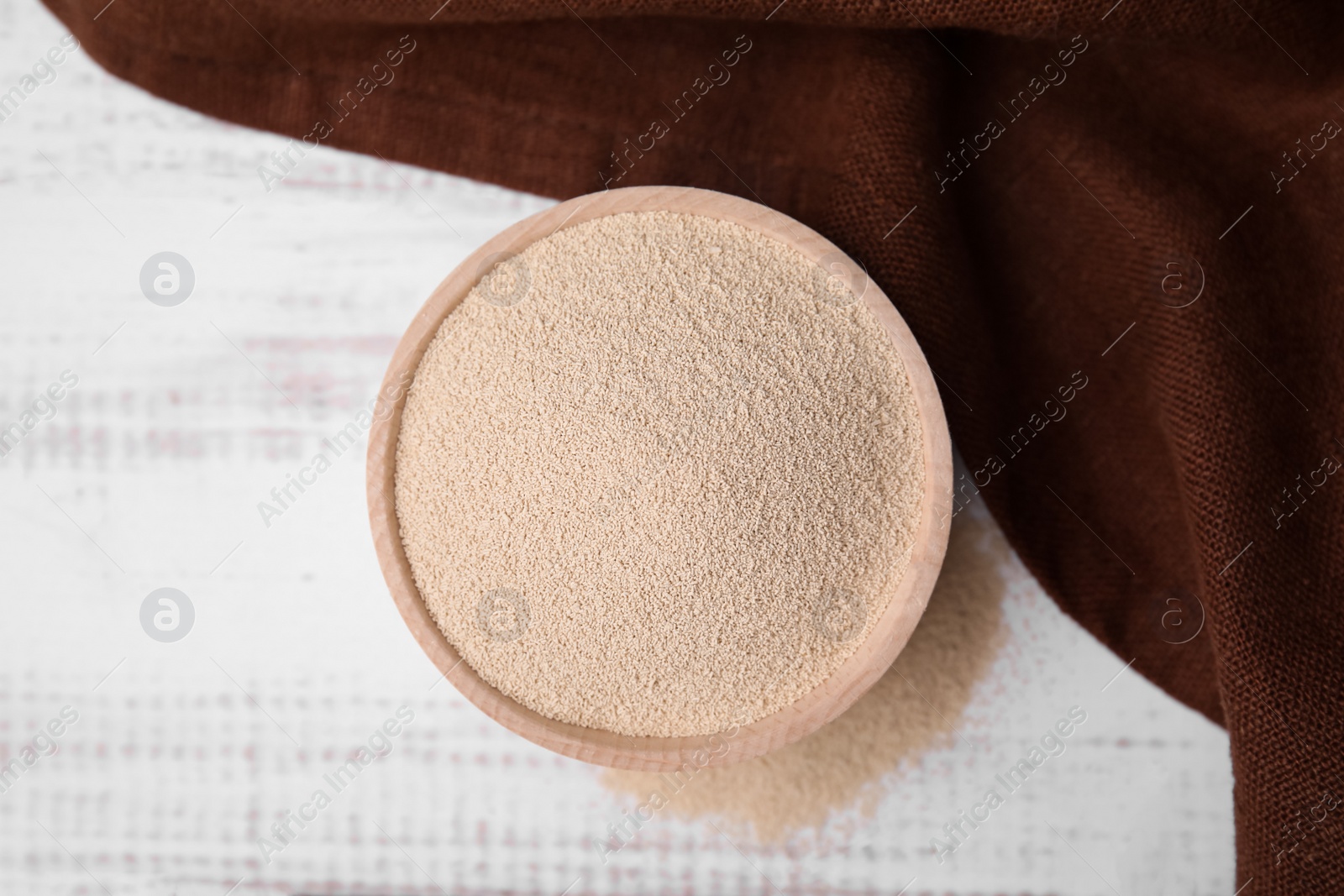 Photo of Granulated yeast in bowl on white wooden table, top view