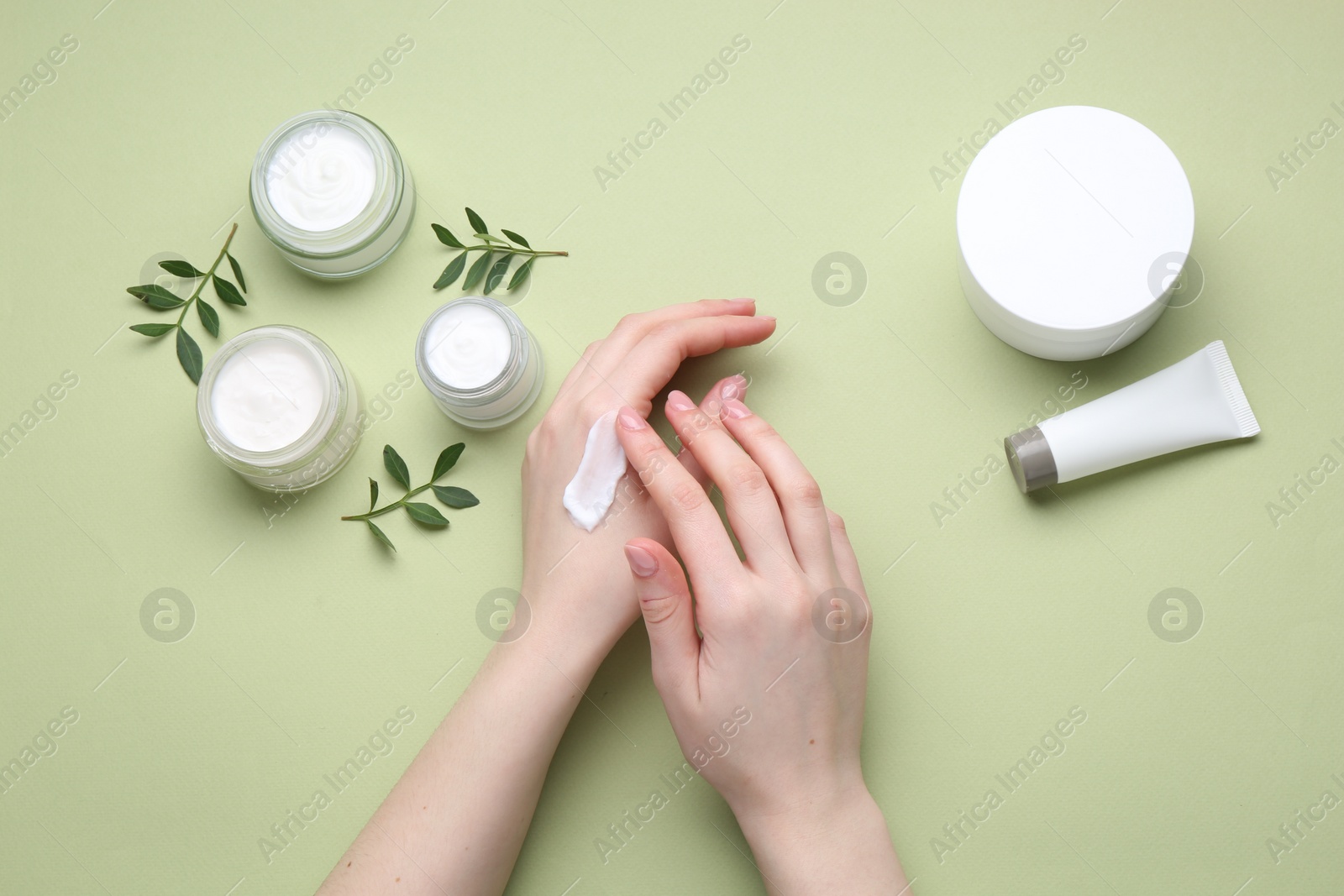 Photo of Woman applying hand cream on green background, top view