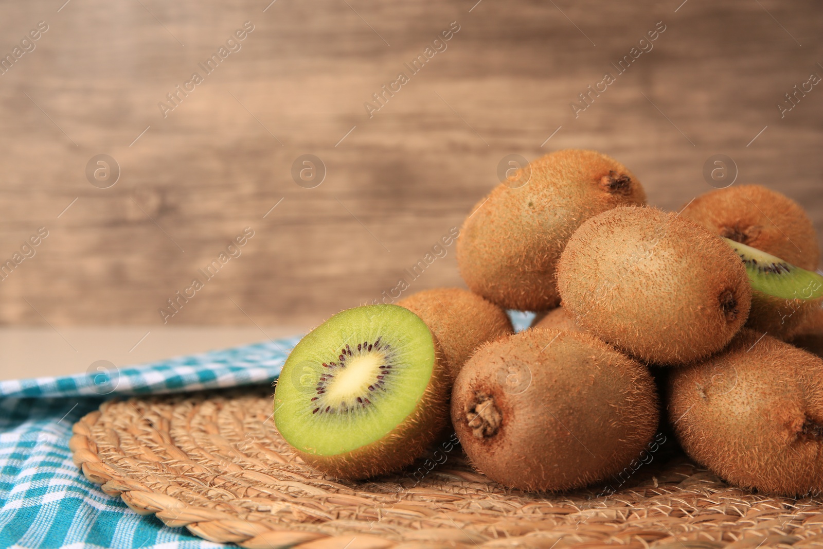Photo of Heap of whole and cut fresh kiwis on wicker mat, space for text