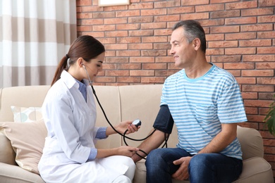 Photo of Doctor visiting mature man at home. Measuring blood pressure and checking pulse
