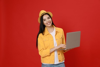 Young woman with modern laptop on red background