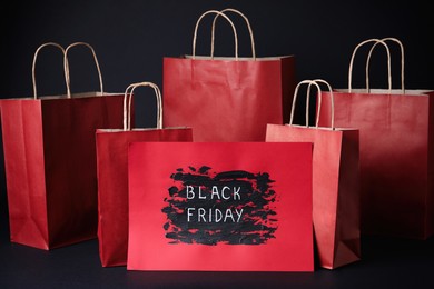 Photo of Red shopping bags and card with text Black Friday on dark background