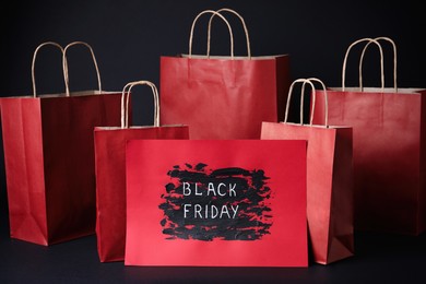 Red shopping bags and card with text Black Friday on dark background