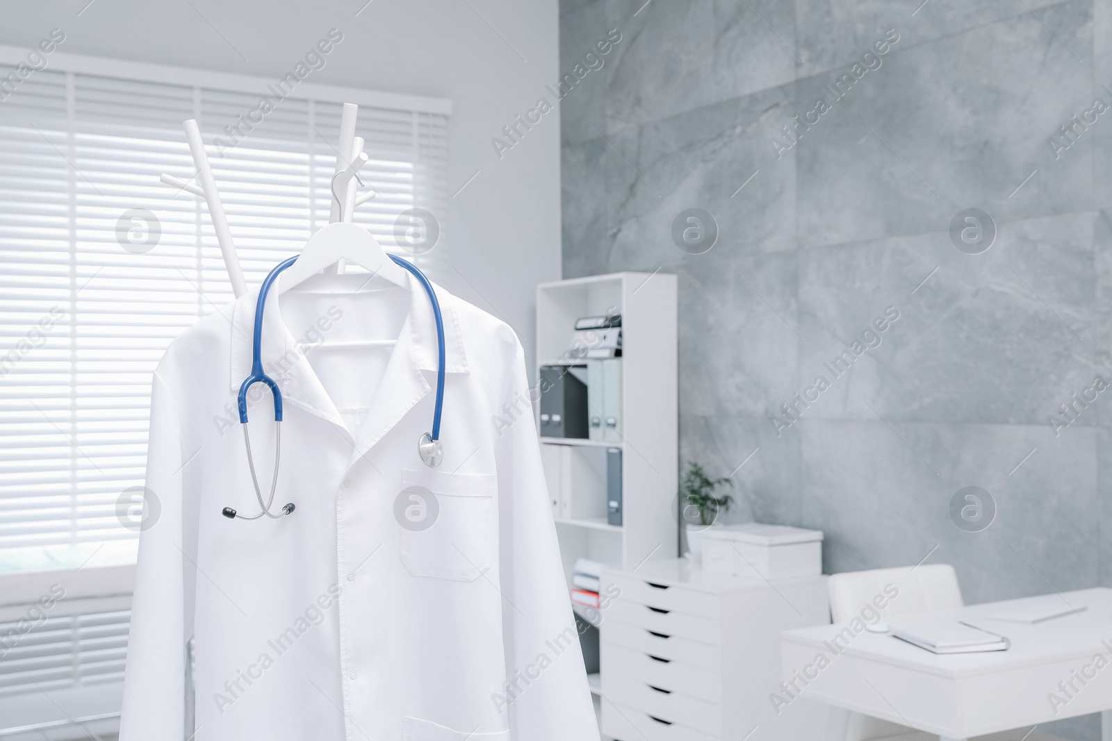 Photo of White doctor's gown and stethoscope hanging on rack in clinic. Space for text