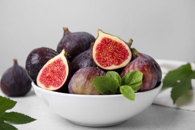 Bowl of tasty ripe figs and green leaves on light table, closeup