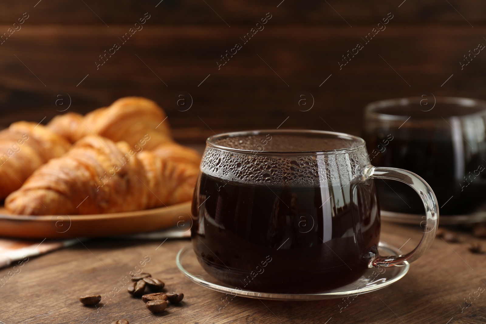 Photo of Hot coffee in glass cup and beans on wooden table, closeup