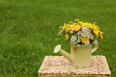Photo of Pale yellow watering can with beautiful flowers on wicker box outdoors, space for text