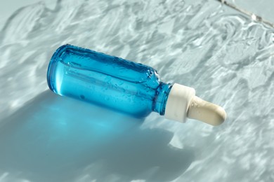 Photo of Wet bottle of cosmetic serum on light blue background