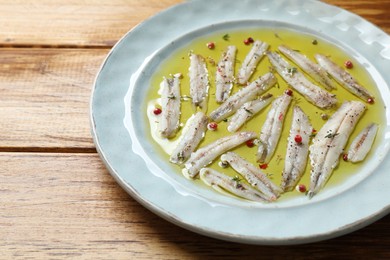 Photo of Tasty pickled anchovies with spices on wooden table, closeup. Space for text