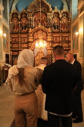 Photo of Stryi, Ukraine - September 11, 2022: Parents with child during baptism ceremony in Assumption of Blessed Virgin Mary cathedral, back view