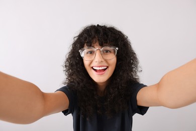 Photo of Beautiful young woman in eyeglasses taking selfie on light grey background