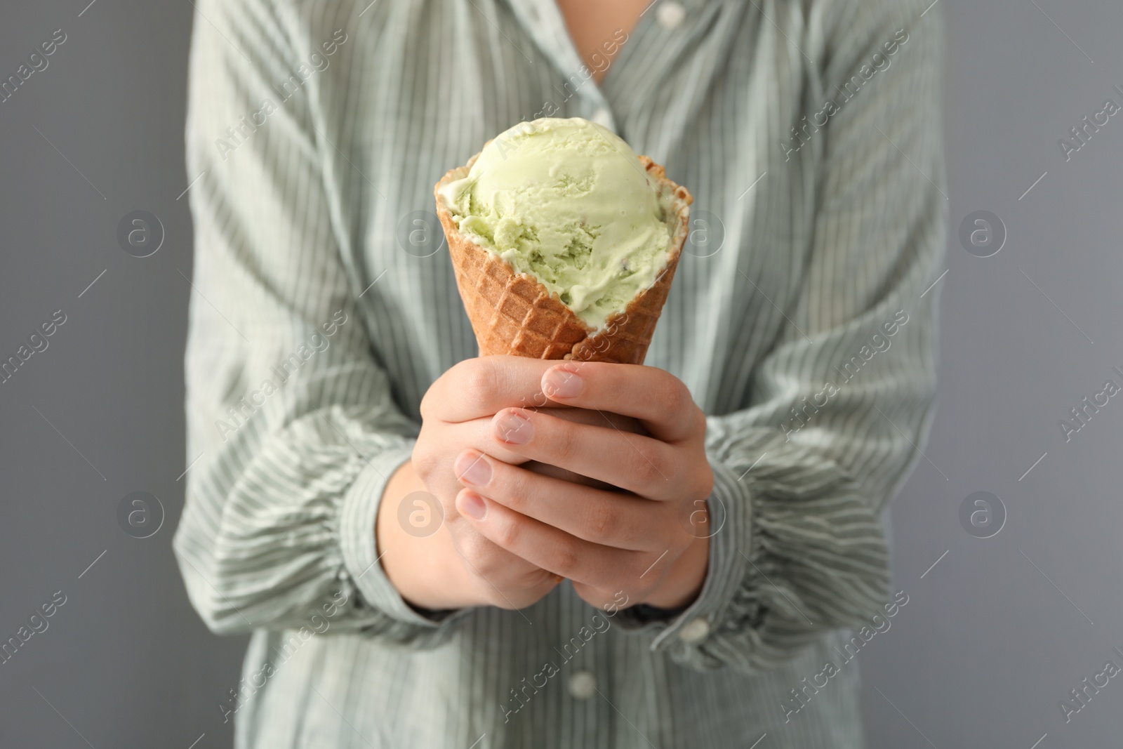 Photo of Woman holding green ice cream in wafer cone on grey background, closeup