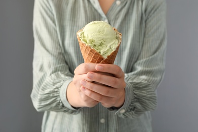 Photo of Woman holding green ice cream in wafer cone on grey background, closeup
