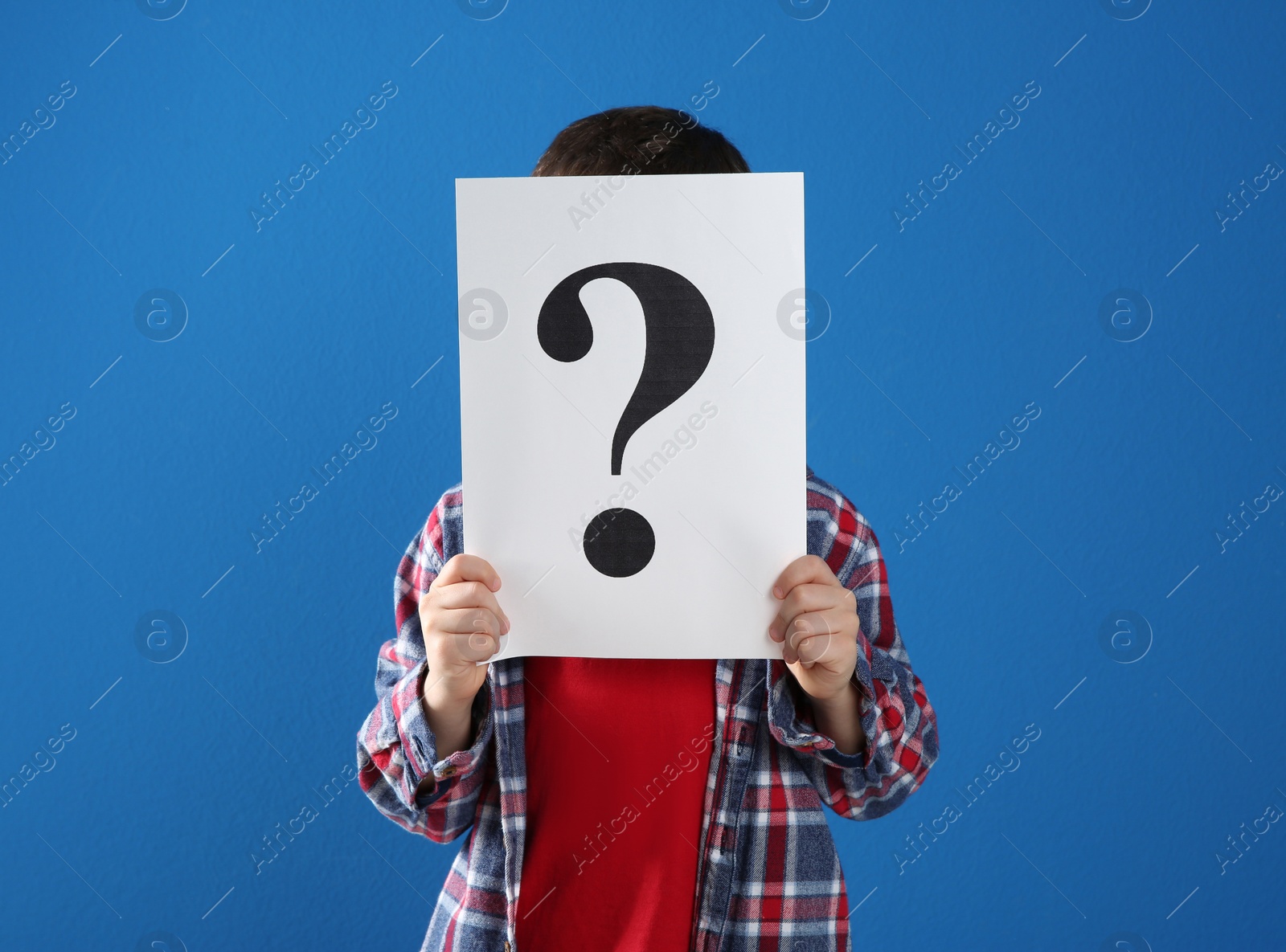 Photo of Little boy holding paper with question mark on blue background