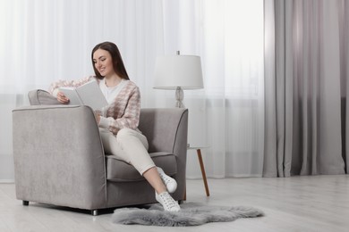 Woman reading book in armchair near window with stylish curtains at home. Space for text