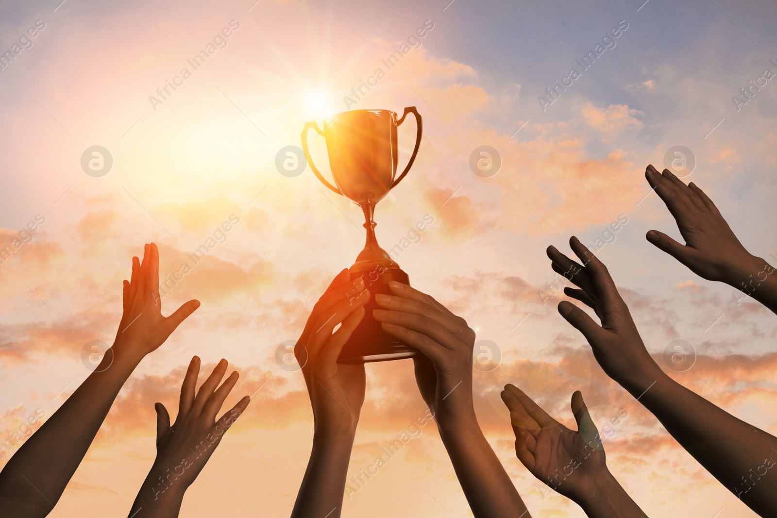 Image of Winning team with gold trophy cup against shining sun in sky 