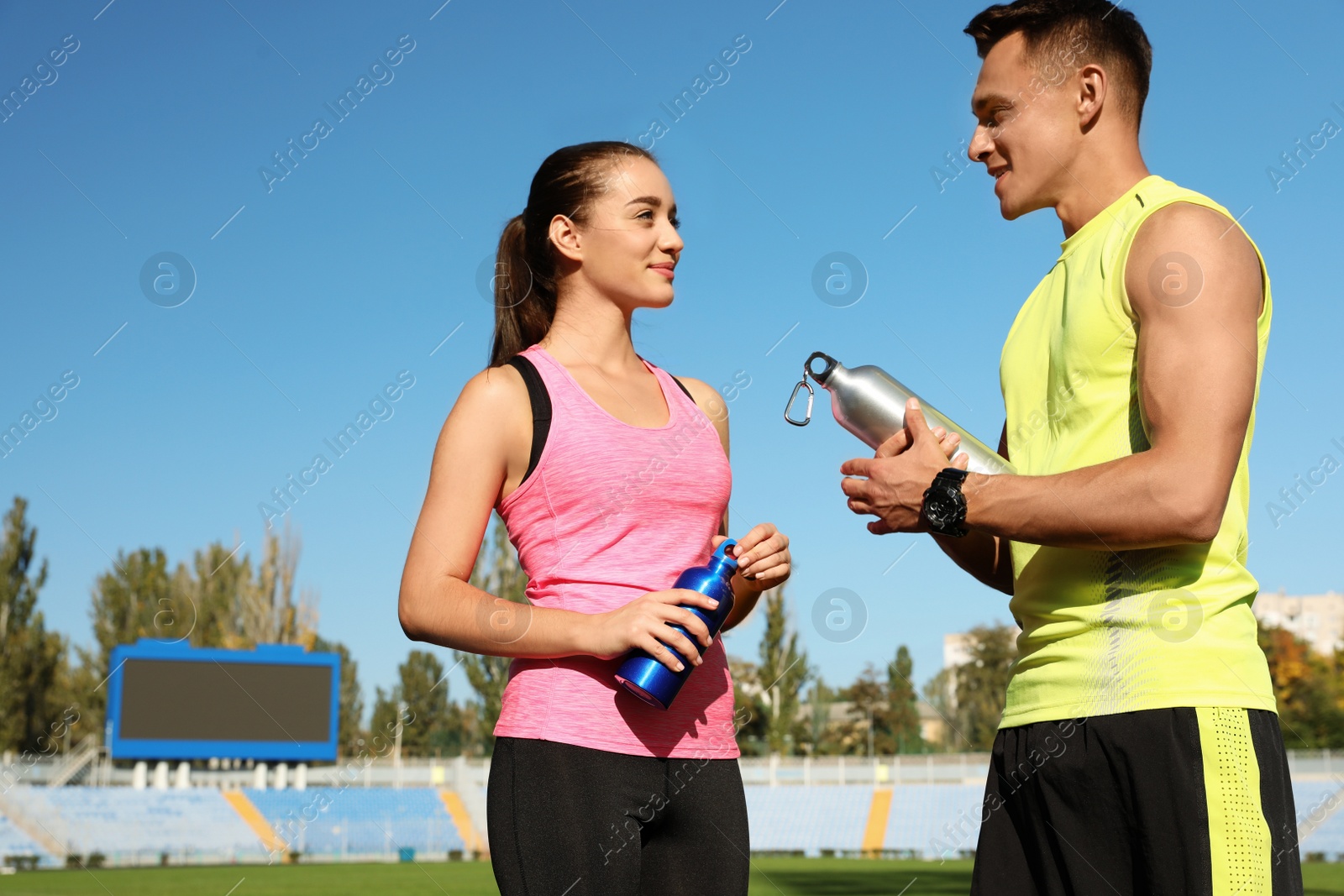 Photo of Young sporty couple holding bottles of water at stadium on sunny day