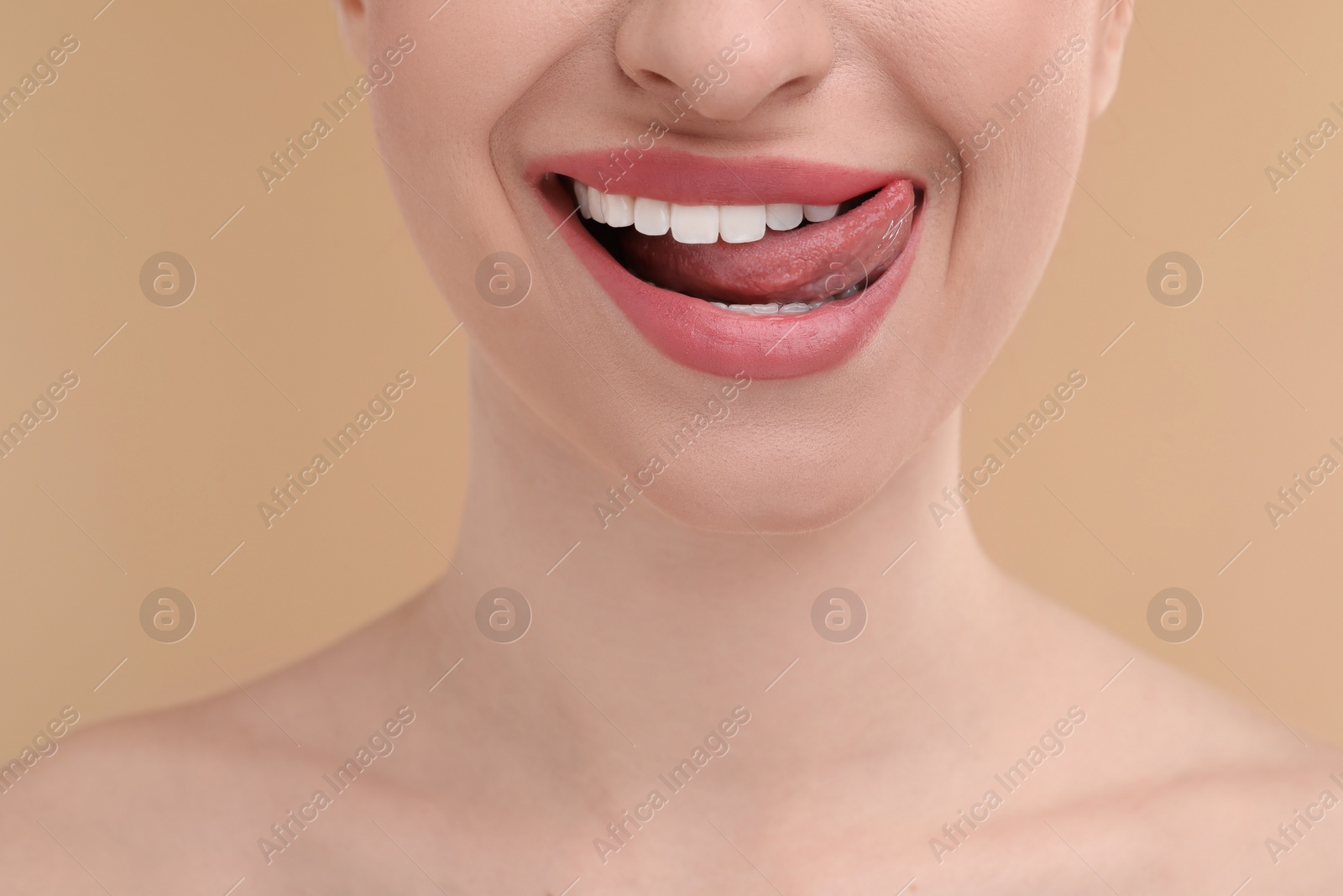 Photo of Young woman licking her teeth on beige background, closeup