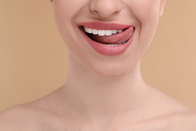 Young woman licking her teeth on beige background, closeup