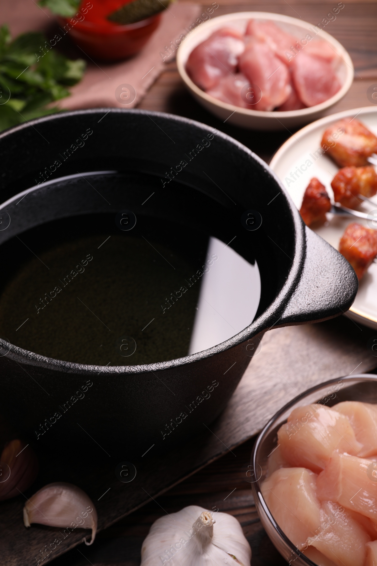 Photo of Fondue pot, forks with fried meat pieces and other products on wooden table