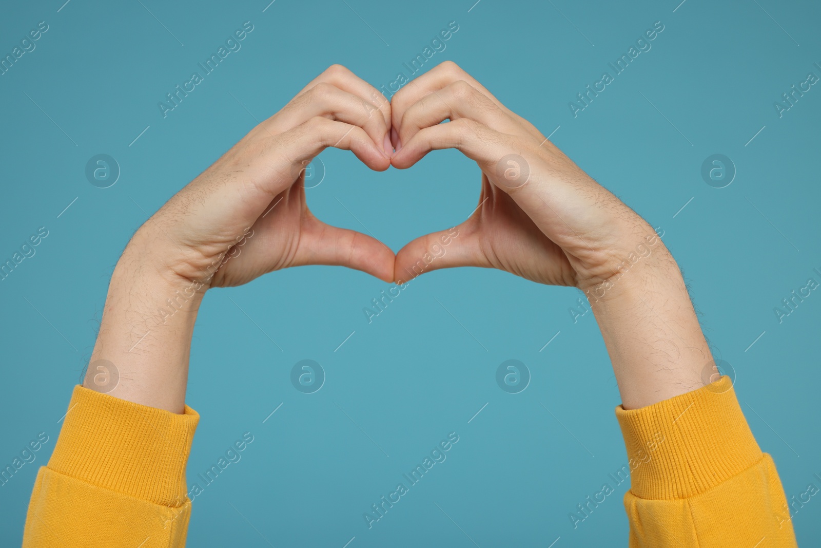 Photo of Man showing heart gesture with hands on light blue background, closeup