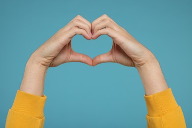 Man showing heart gesture with hands on light blue background, closeup