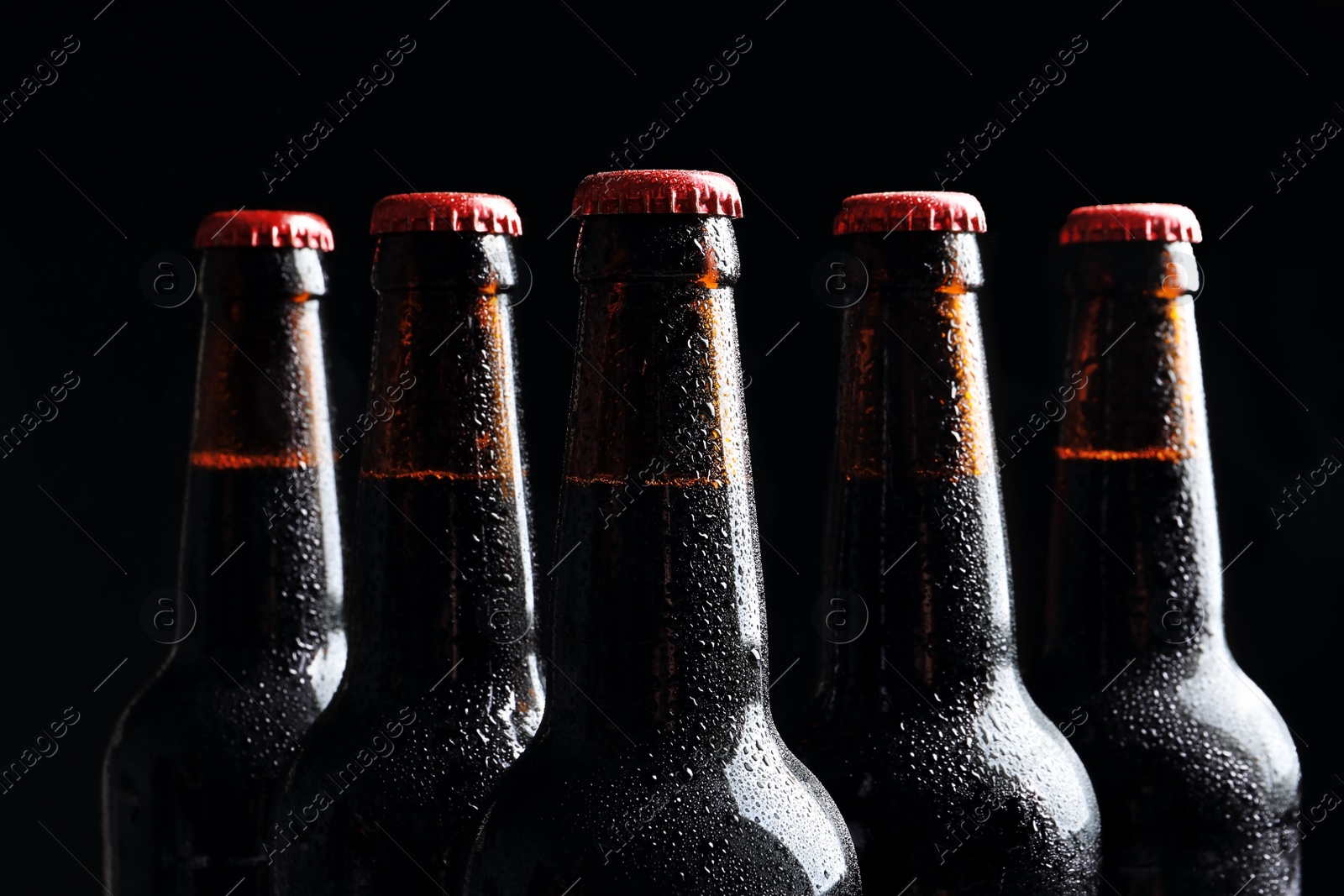 Photo of Bottles of tasty cold beer on black background, closeup