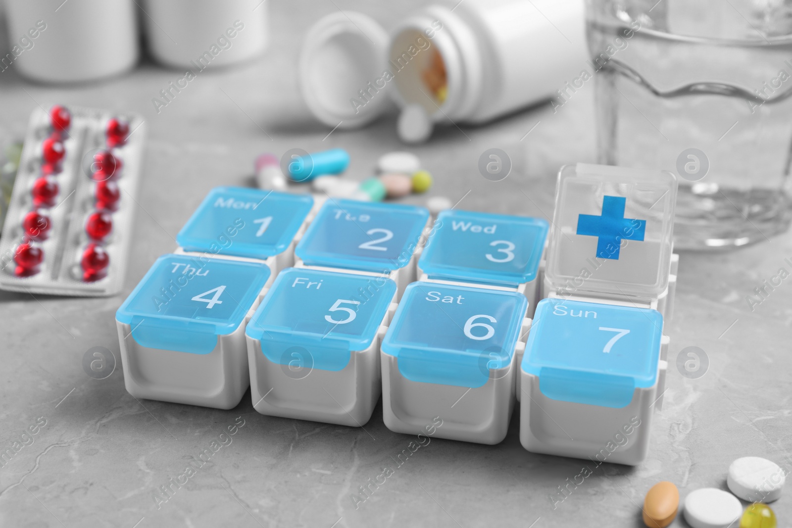 Photo of Weekly pill box with medicaments on grey marble table, closeup
