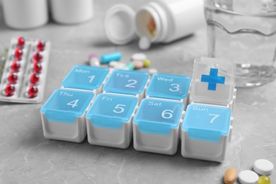Photo of Weekly pill box with medicaments on grey marble table, closeup