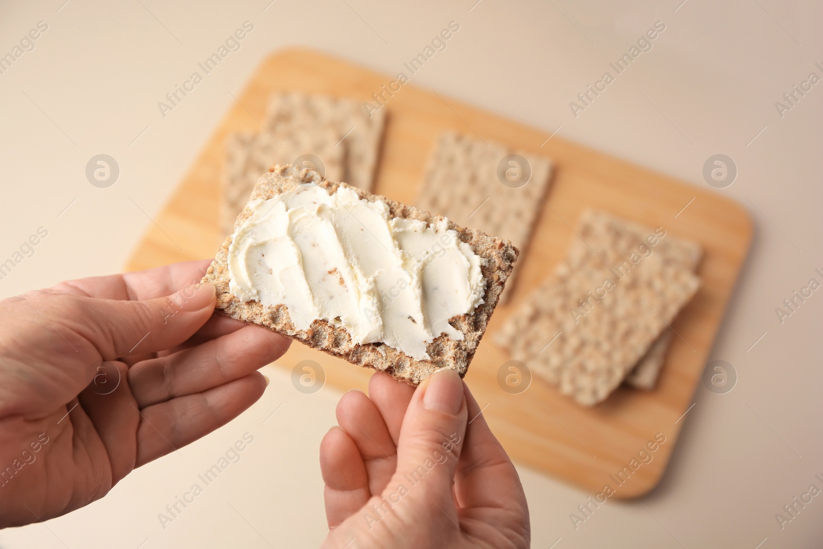 Photo of Woman holding fresh crunchy crispbread with cream cheese above table, closeup. Space for text