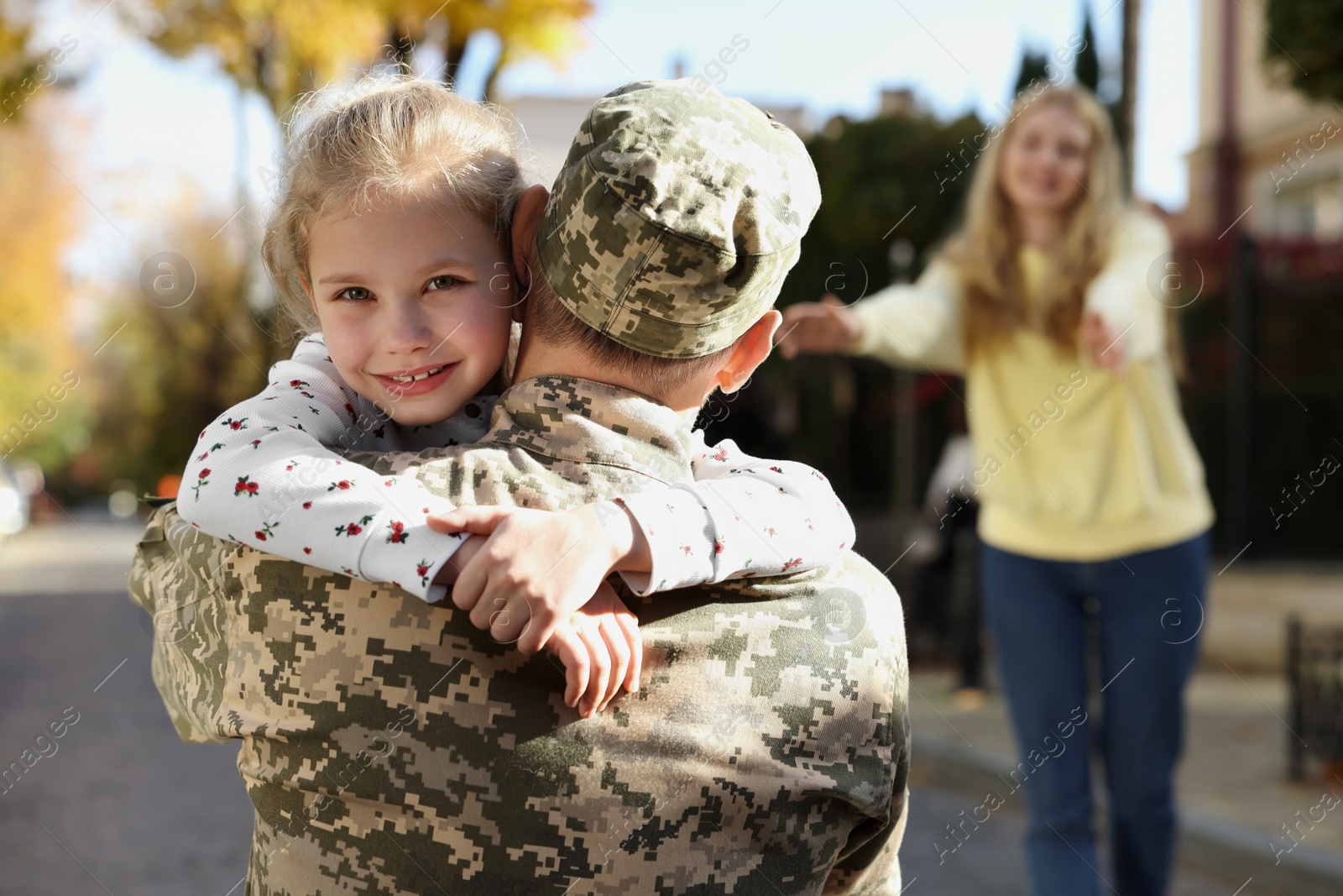 Photo of Daughter hugging her father in Ukrainian military uniform on city street. Family reunion