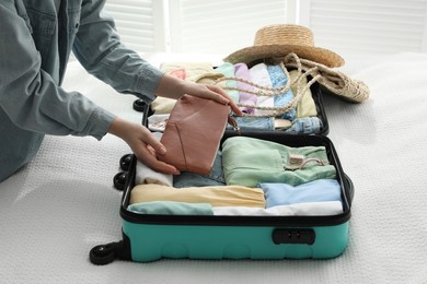 Photo of Woman packing suitcase for trip on bed, closeup