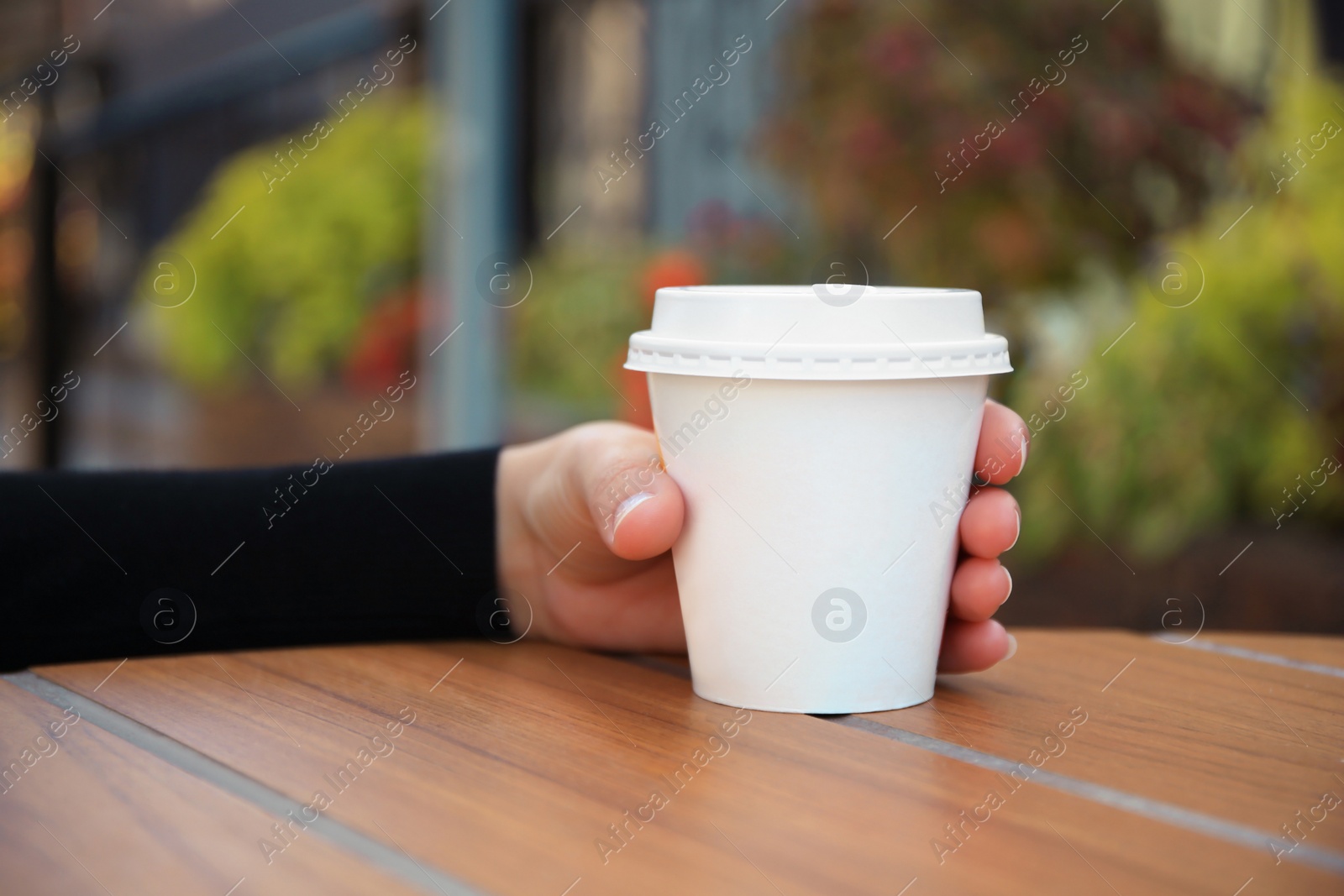 Photo of Woman with cardboard cup of coffee at table outdoors, closeup