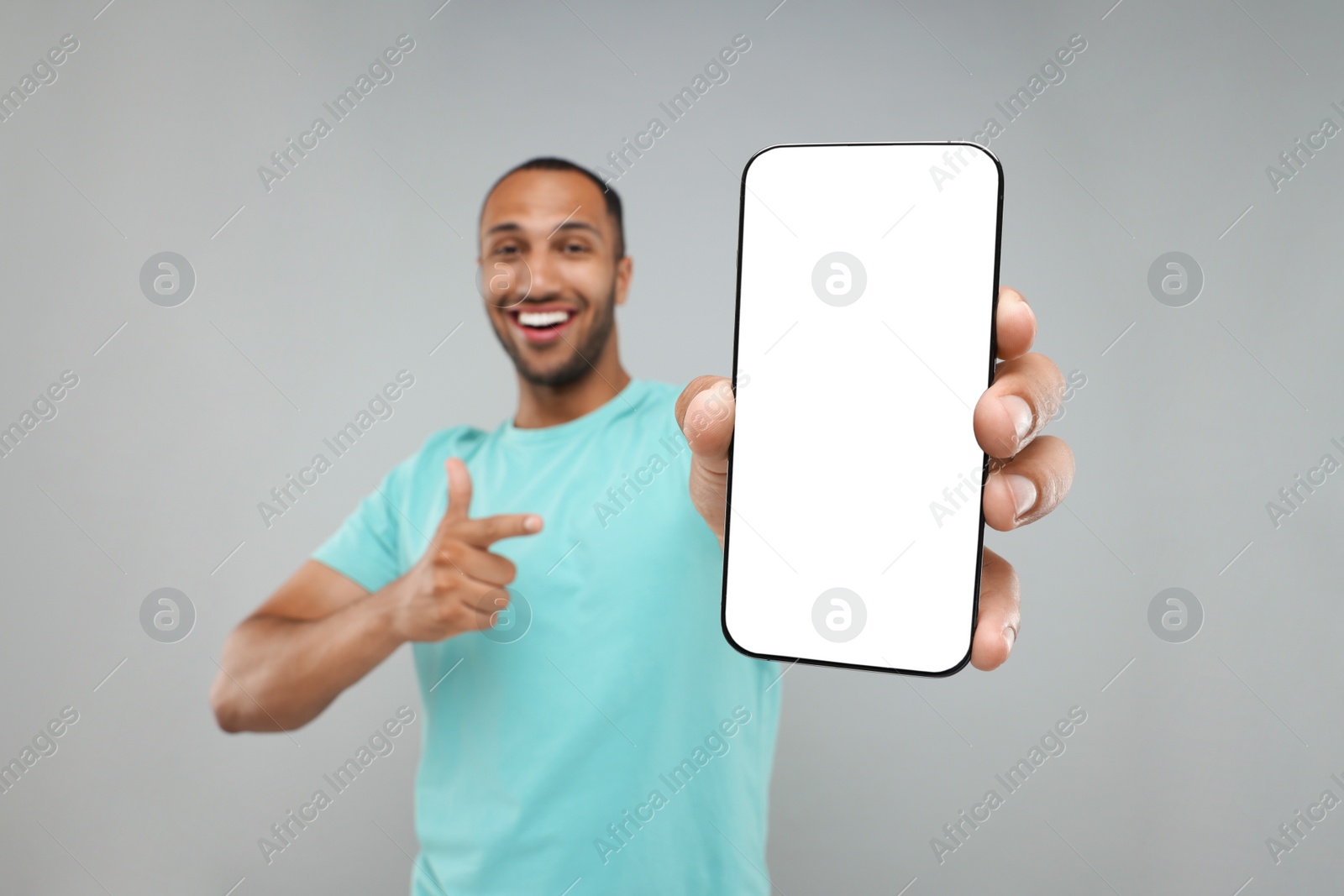 Photo of Young man showing smartphone in hand and pointing at it on light grey background, selective focus. Mockup for design