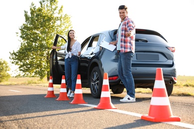 Photo of Instructor with clipboard and his student near car outdoors. Driving school exam