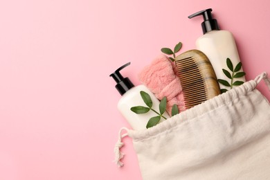 Photo of Preparation for spa. Compact toiletry bag with different cosmetic products and twigs on pink background, flat lay. Space for text