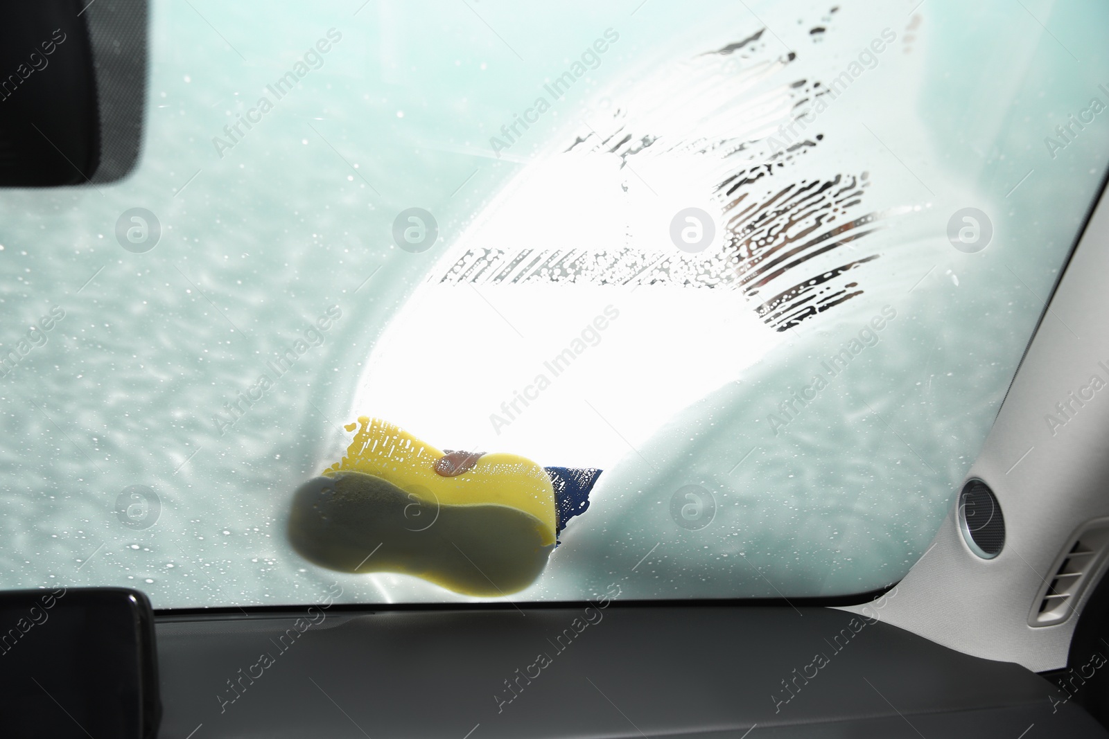 Photo of Worker cleaning automobile windshield with sponge at car wash, view from inside