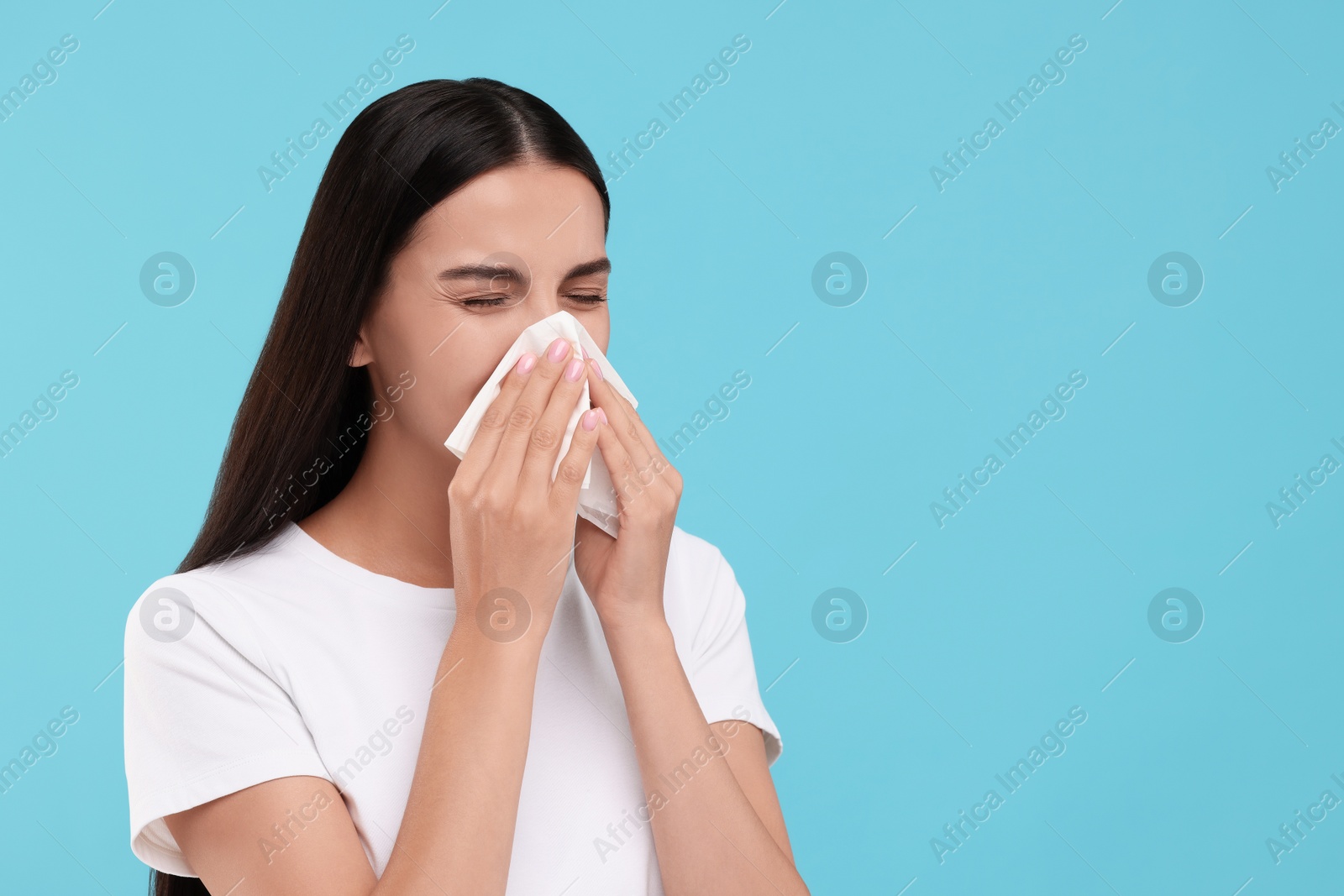 Photo of Suffering from allergy. Young woman blowing her nose in tissue on light blue background. Space for text