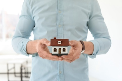 Male real estate agent with house model indoors, closeup