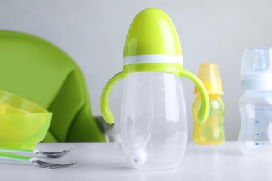 Photo of Plastic baby bottle, spoon and fork on white table indoors